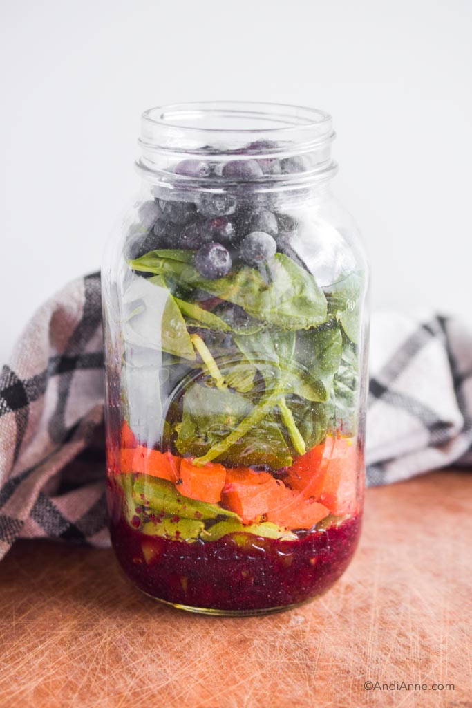 antioxidant salad in mason jar with blueberry dressing, chopped vegetables and blueberries. A kitchen towel is behind the jar.