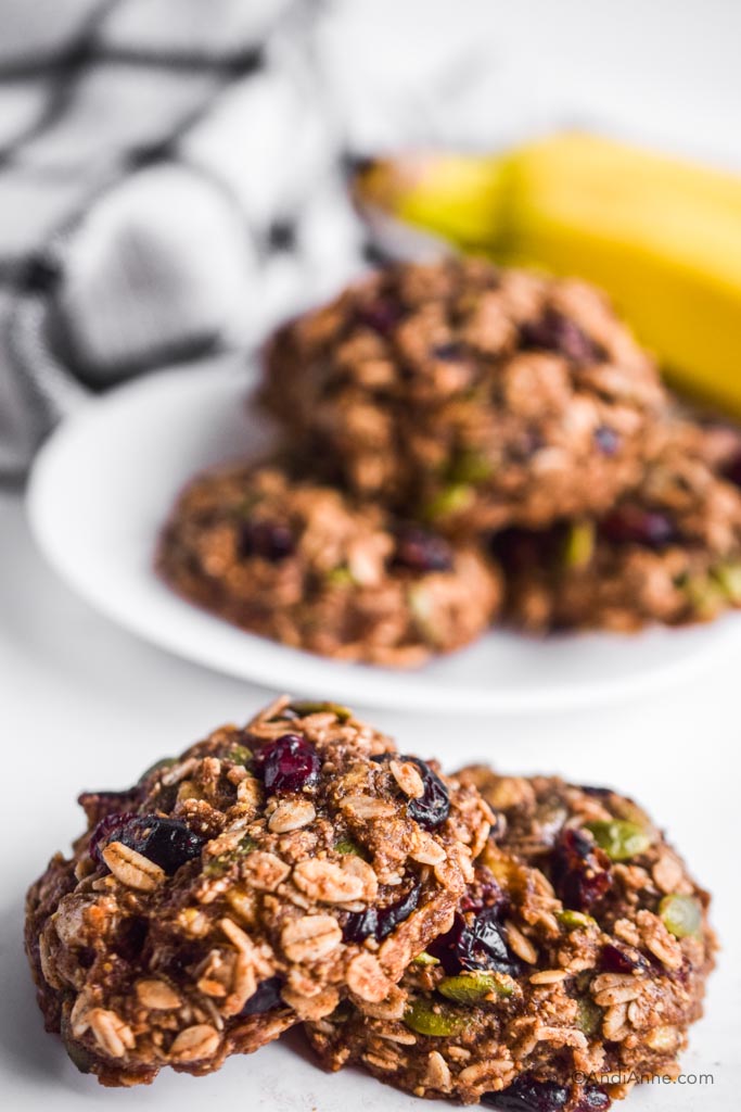 banana cranberry breakfast cookies stacked on eachother with white plate and kitchen towel in background