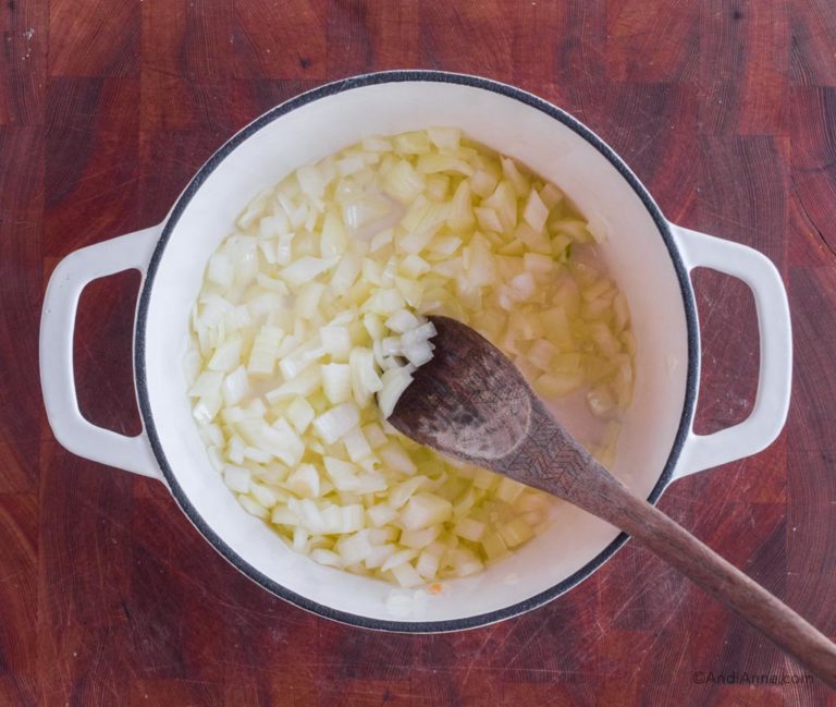 sauteed onions in a white dutch oven with wooden spoon.