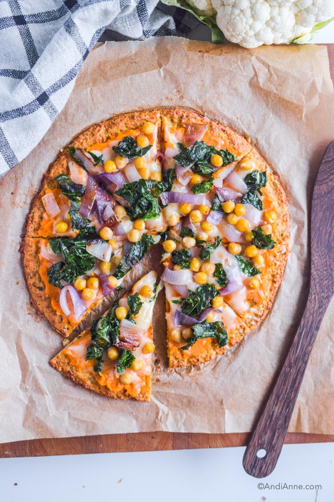 kale chickpea cauliflower pizza on parchment paper with wooden spoon beside it
