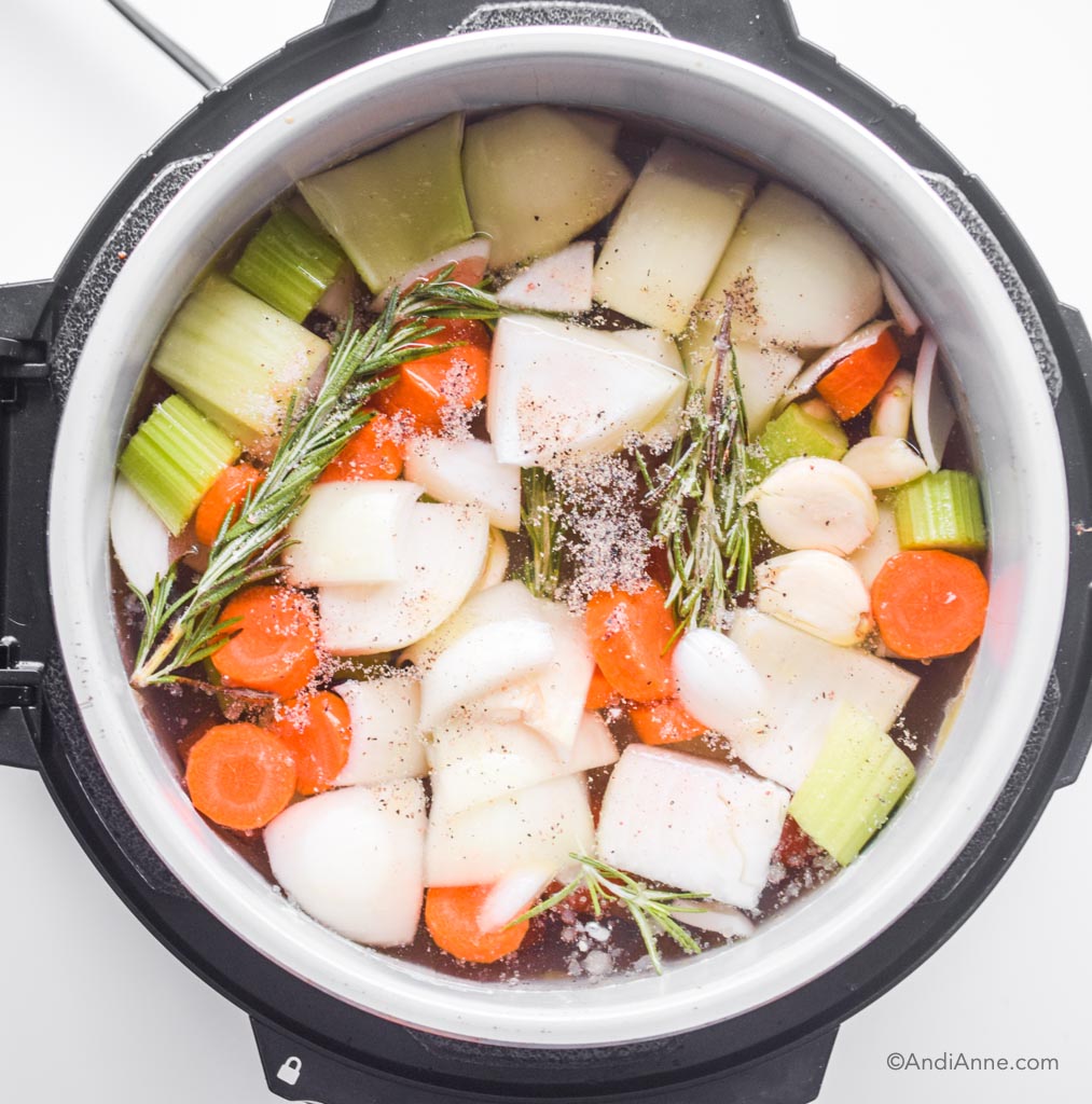 Looking down into an instant pot with raw vegetables, rosemary sprigs, ground pepper, and filled with water before it's sealed to cook.