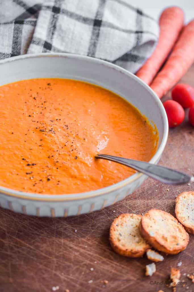 Side angle of bowl of carrot tomato soup. Crackers are piled in the front of the bowl.