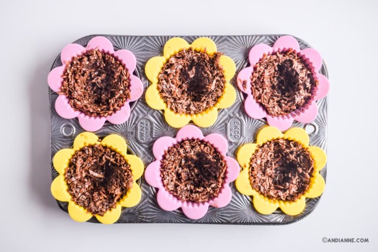 flower shape pink and yellow silicone muffin cups inside a tin muffin pan with shredded coconut mixture inside each