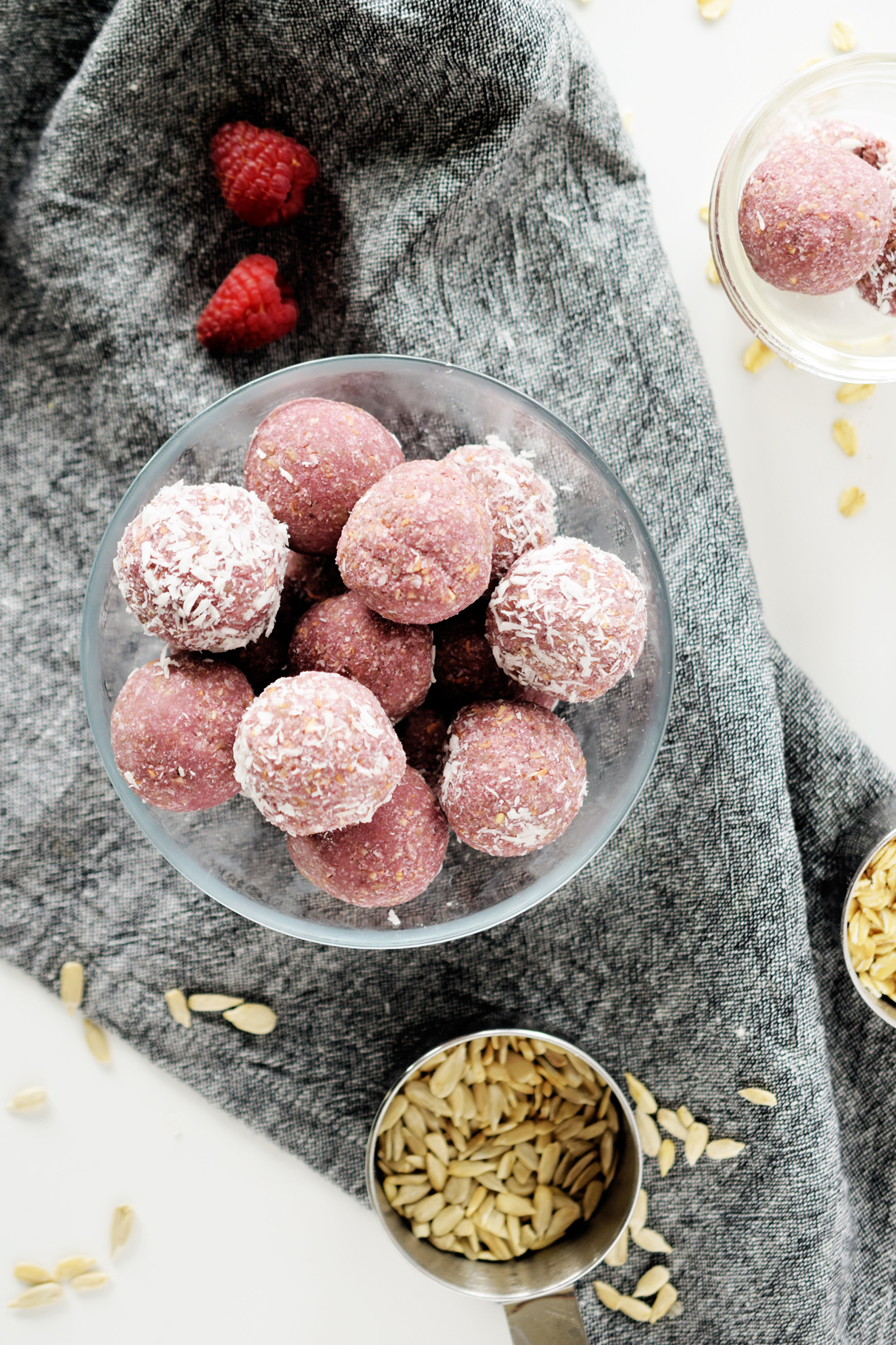 raspberry coconut energy balls in glass bowl with grey napkin and pumpkin seeds sprinkled from a cup
