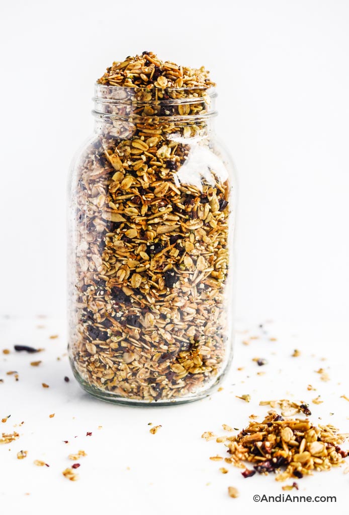 homemade superfood granola poured into a large glass jar and sprinkled on the white counter surrounding jar