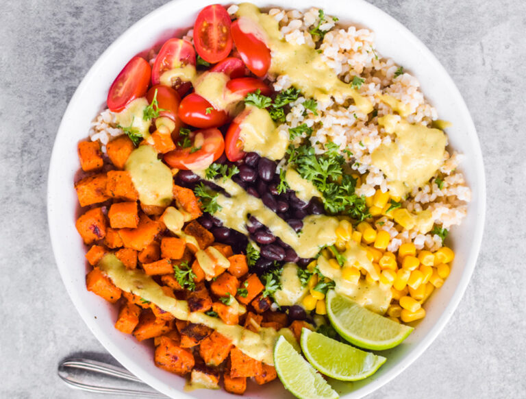 Sweet potato taco bowl with limes, a fork and dressing drizzled on top.