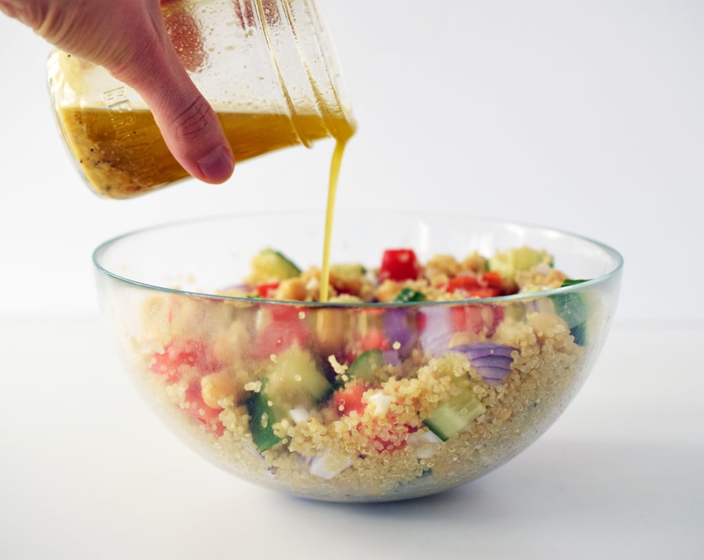honey dijon quinoa salad in glass bowl with salad dressing being poured over top out of a mason jar
