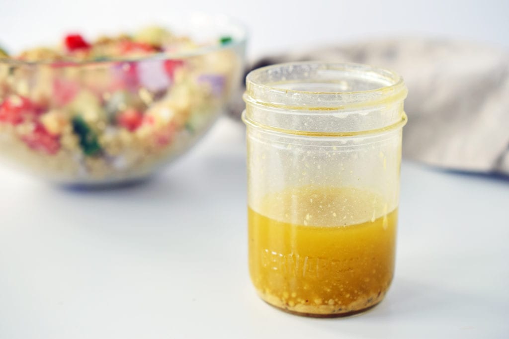 honey dijon mustard in a mason jar with bowl of quinoa salad in the background