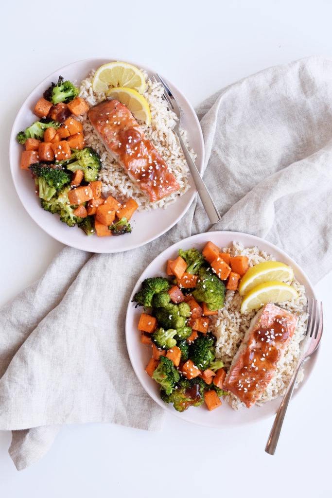 cooked teriyaki salmon with broccoli and sweet potato on two plates with rice and forks