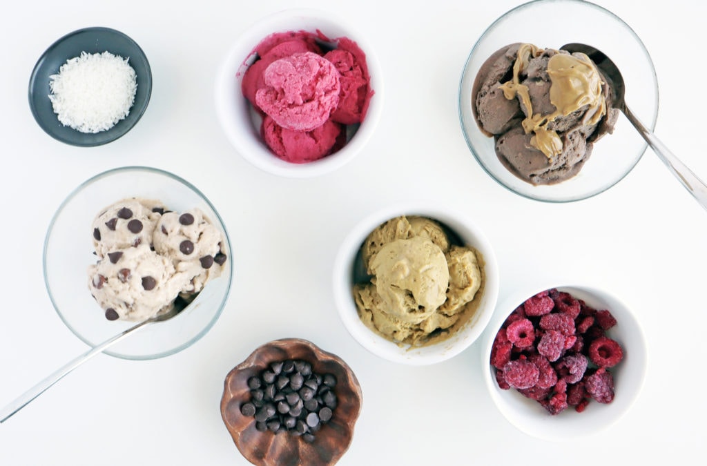 ingredients like shredded coconut, chocolate chips and frozen raspberries in bowls around banana nice cream bowls