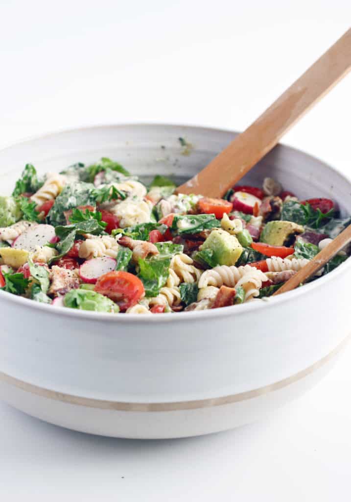 mixing BLT pasta salad with wooden spoons