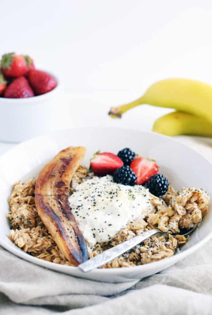 creamy morning oatmeal in white bowl with spoon and fried banana. Beige napkin in foreground.