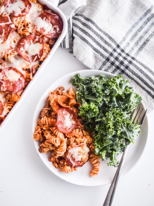 pizza pasta bake on a white plate with kale salad and a fork