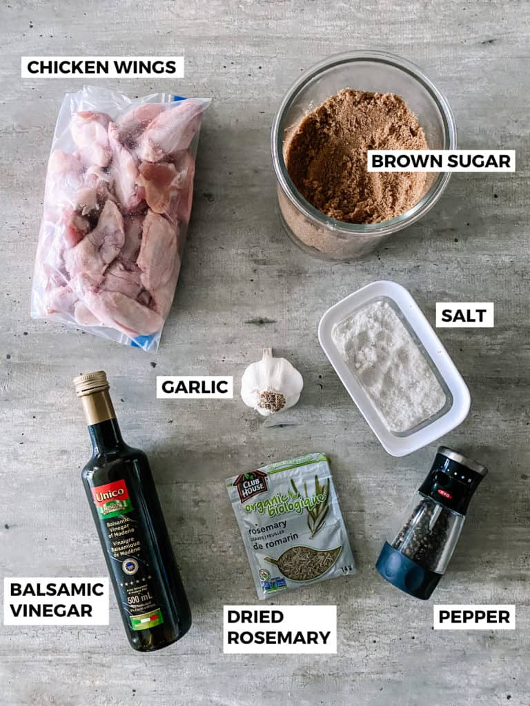 Ingredients to make recipe including raw chicken wings in a bag, brown sugar, balsamic vinegar, dried rosemary and pepper.
