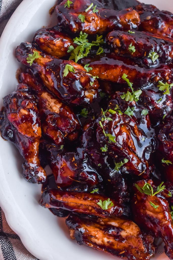 Balsamic glazed chicken wings sprinkled with a bit of chopped parsley in a white dish.