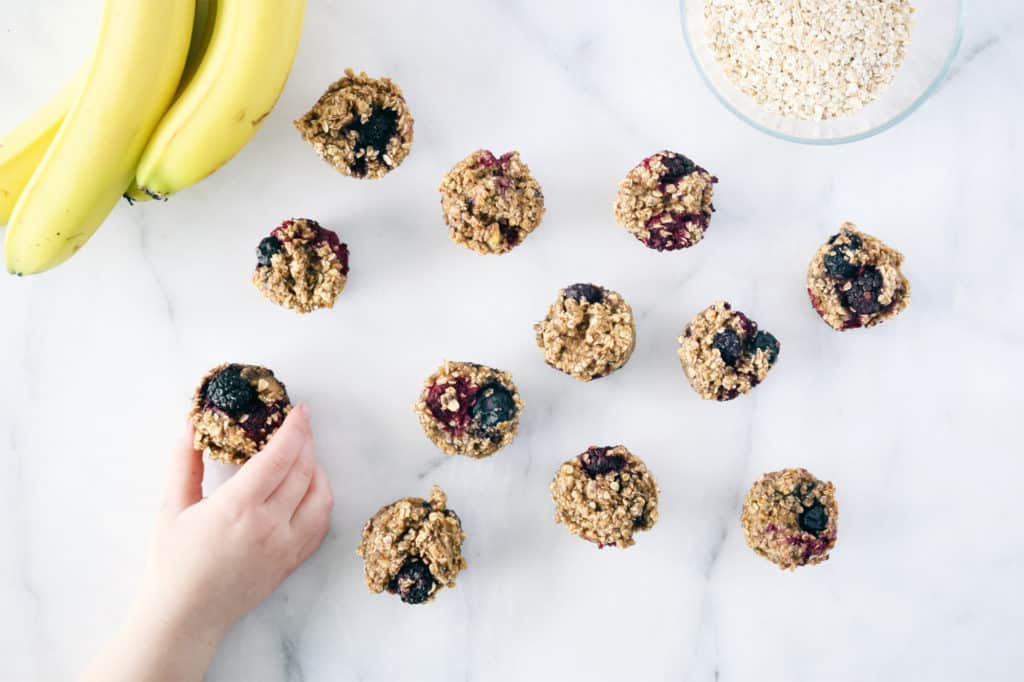 oat berry mini muffins on counter with toddler hand grabbing one. bananas in top corner.