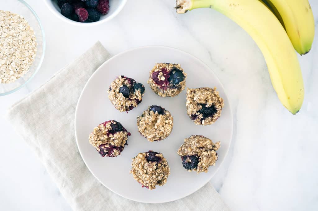 mini muffins on a grey plate with beige napkin. Bananas and oats in top corner.