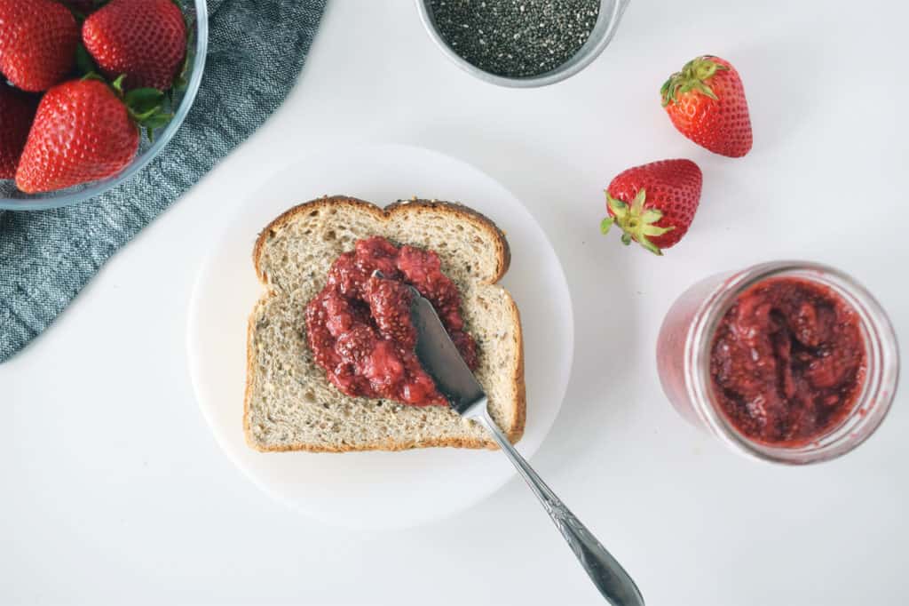 jam spread on toast. Fresh strawberries and mason jar with jam are surrounding it.