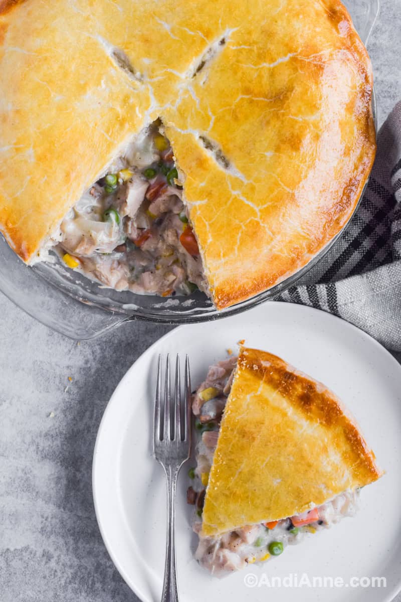 Slice of turkey pie on a white plate with a fork and full pie beside the plate.