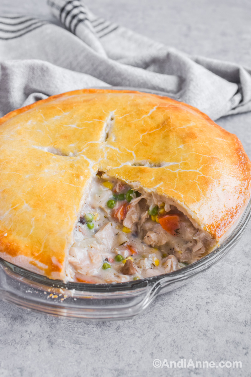 Side angle of turkey pot pie with slice cut out and filling spilling into the pan.