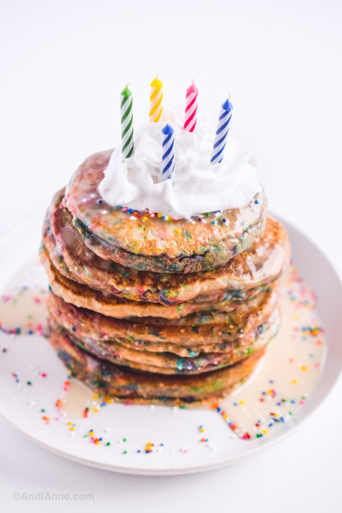 birthday sprinkle pancakes with whipped cream and candles on a white plate