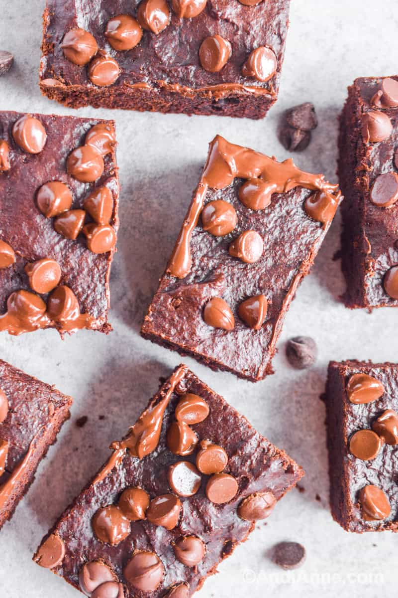 Close up of a few brownies with slightly melted chocolate chips on top and a few chips sprinkled around the brownie squares.