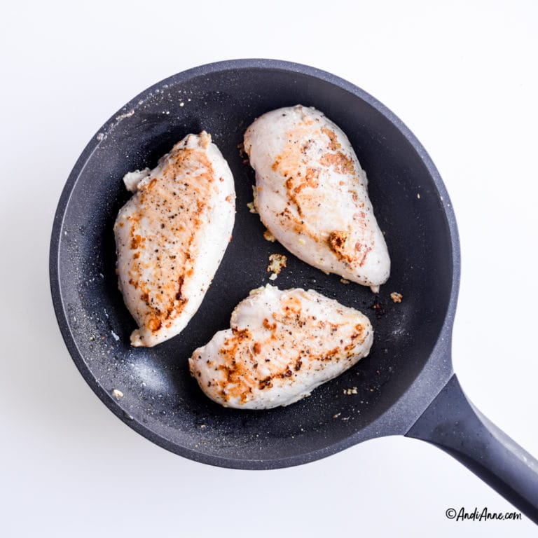 3 chicken breasts in a black frying pan cooking