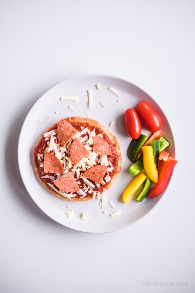 homemade pizza lunchables on a plate with grape tomatoes, chopped bell peppers and sprinkled mozzarella cheese