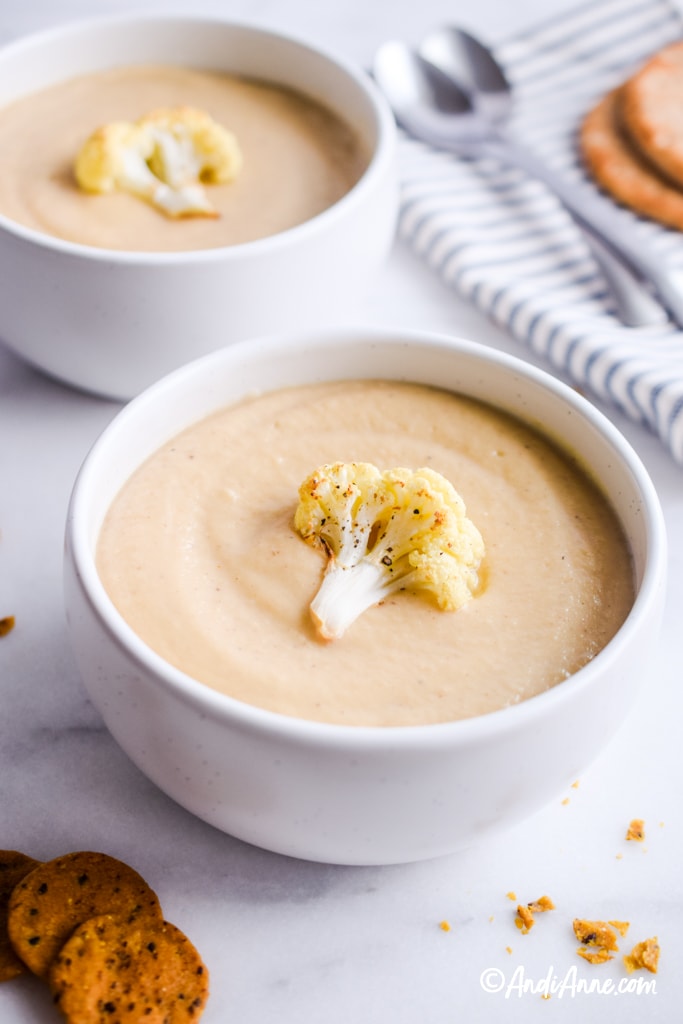 cauliflower soup recipe in white bowls with striped napkin and spoons in background