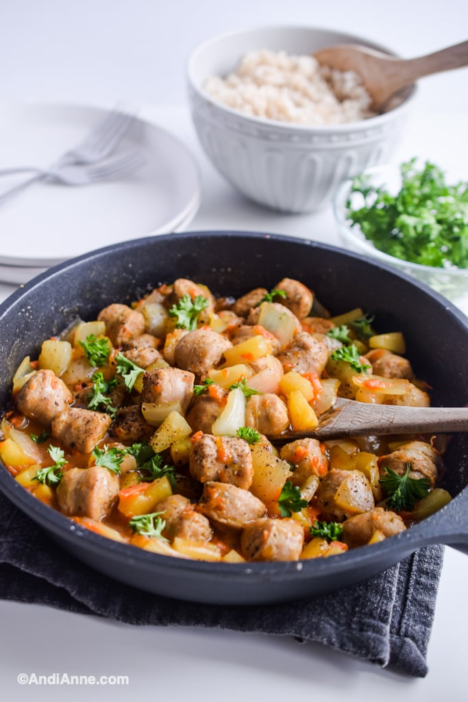 sweet and sour sausage recipe in frying pan with rice in bowl and plates in background