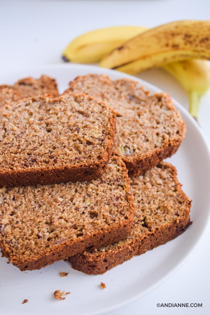 sliced banana bread on white plate with bananas in background