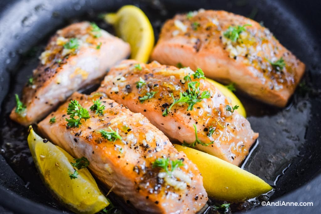 close up detail of honey garlic salmon fillet in a frying pan with lemons