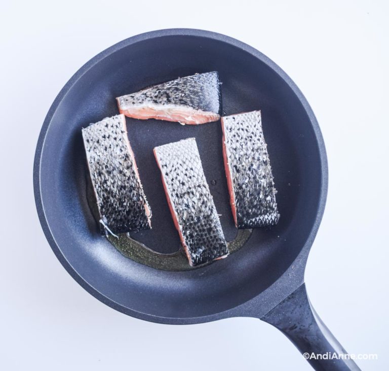 four raw salmon fillets in a frying pan with skin side facing up