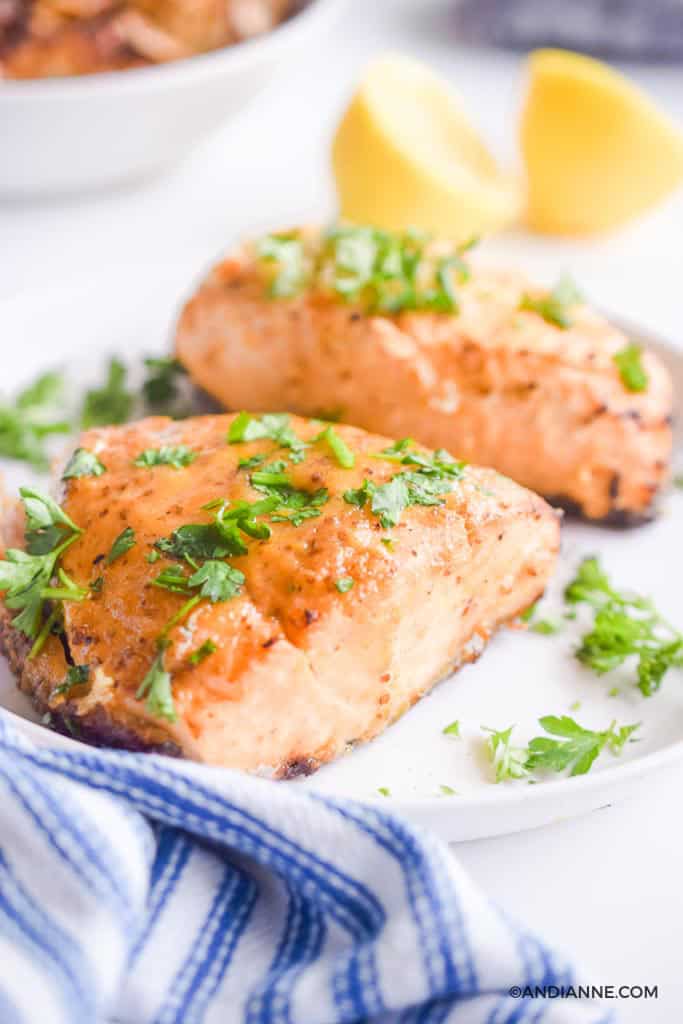 air fryer salmon on white plate sprinkled with chopped parsley. lemons in background. Striped napkin in foreground