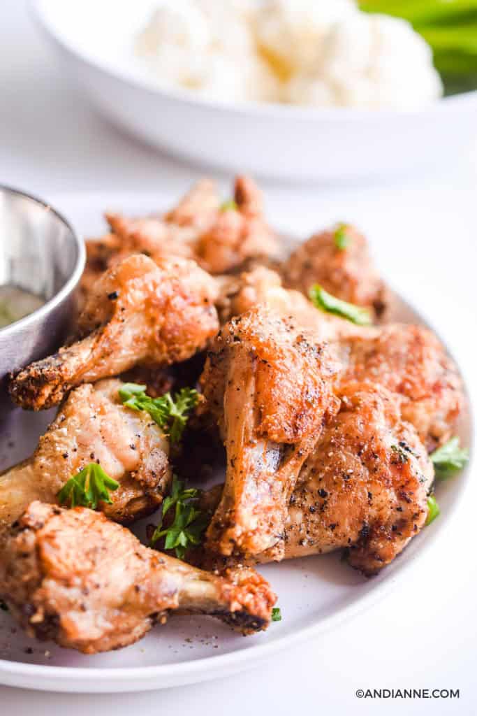 air fryer salt and pepper wings drumettes on white plate with white bowl of cauliflower in background