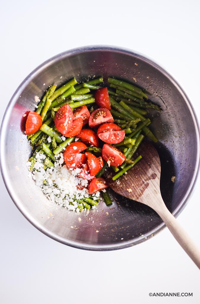 asparagus, tomatoes, feta cheese in a large steel bowl with wooden spoon