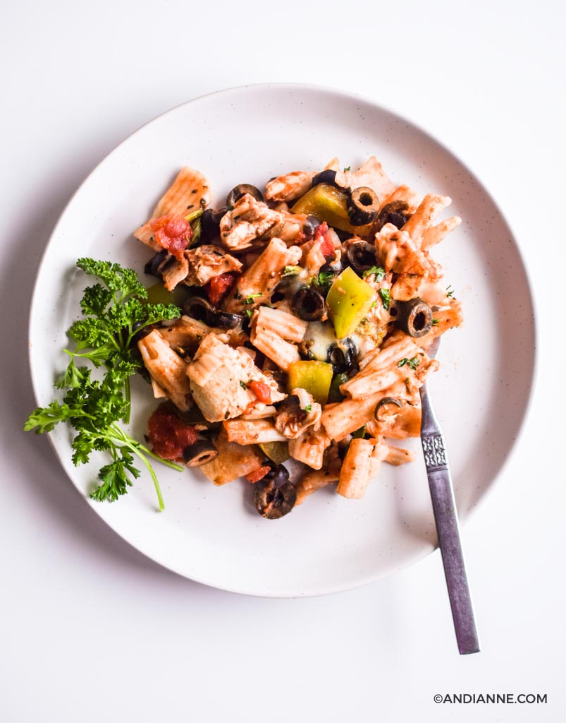 chicken olive pasta bake on a white plate with sprig of parsley and a fork.