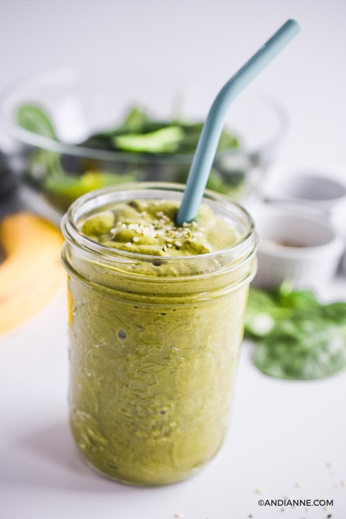 green smoothie in a mason jar with blue straw. Spinach and banana in background.