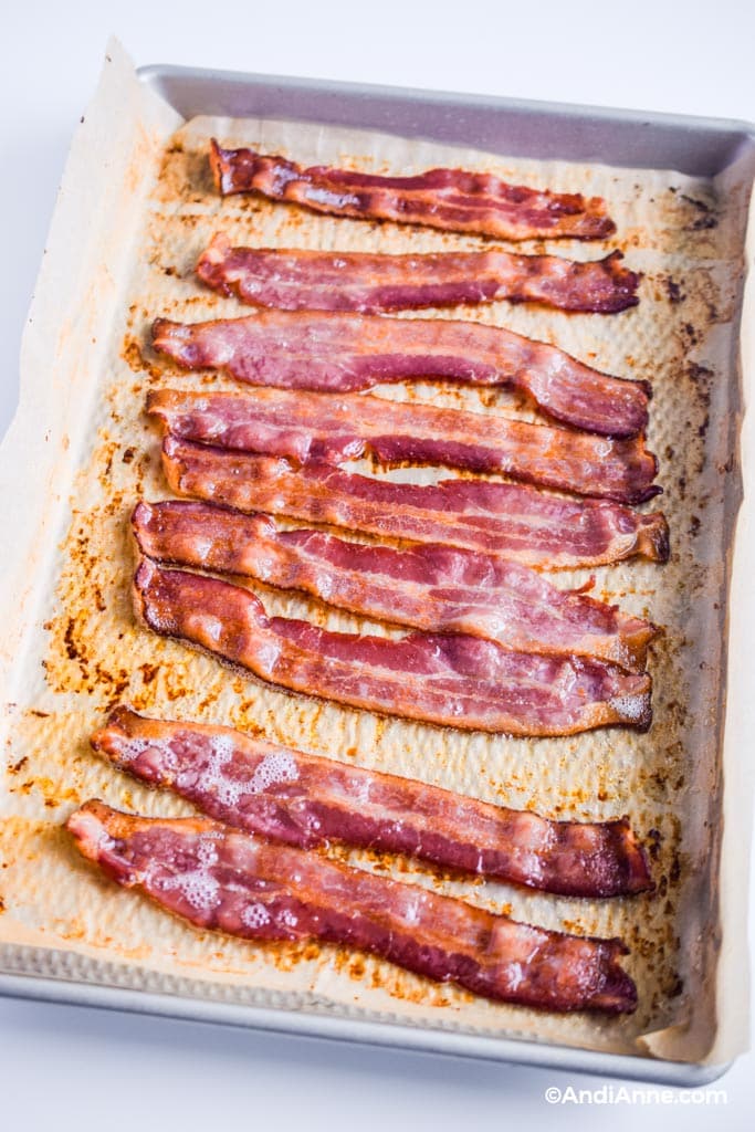 cooked bacon in the oven - bacon on parchment paper on a baking sheet with grease