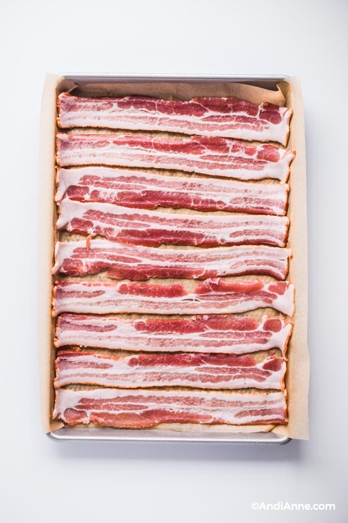 Raw bacon slices on a baking sheet with parchment paper