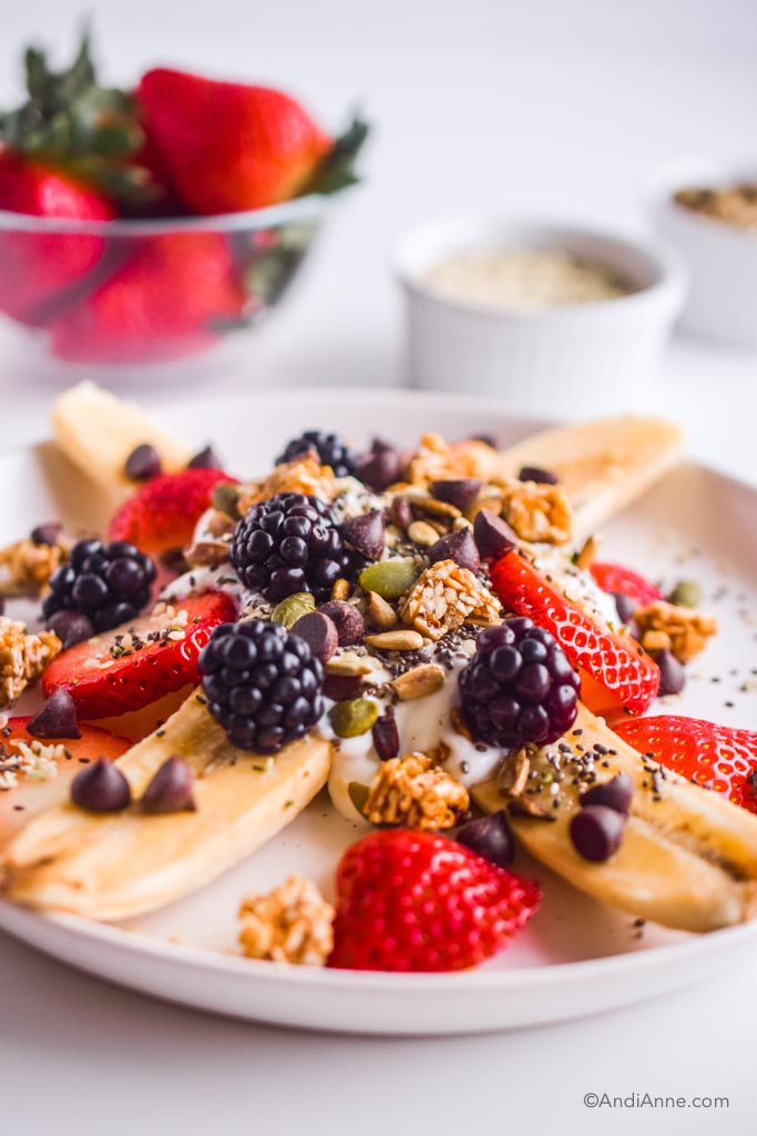 Close up detail of healthy banana split. Details of blackberries, pumpkin seeds, chocolate chips and granola can be seen.