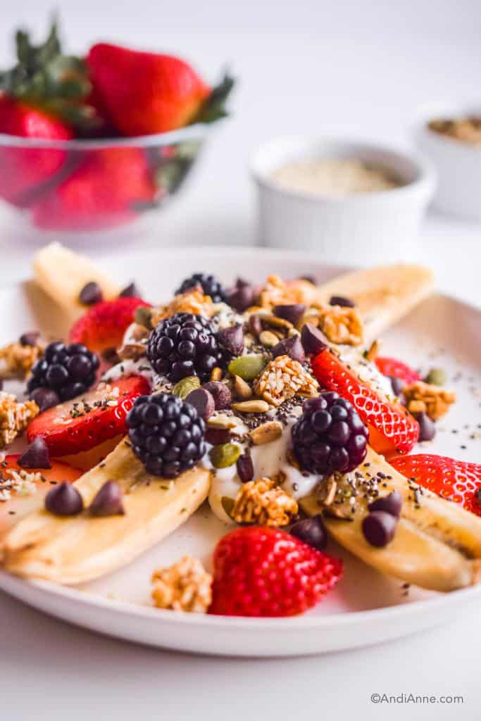 Close up detail of healthy banana split. Details of blackberries, pumpkin seeds, chocolate chips and granola can be seen.