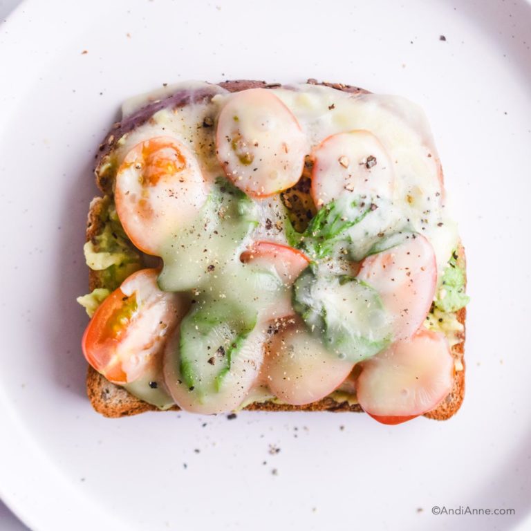 mashed avocado on toast with sliced grape tomatoes, basil and melted white cheese overtop of everything