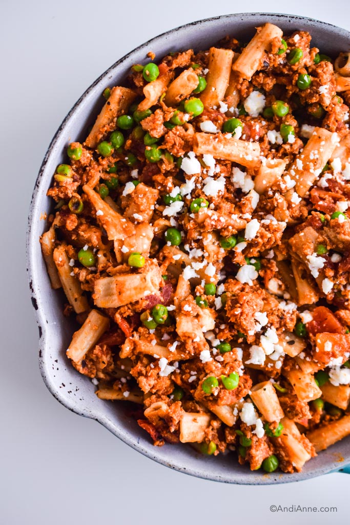 A frying pan with pasta, ground chicken, peas and feta cheese.