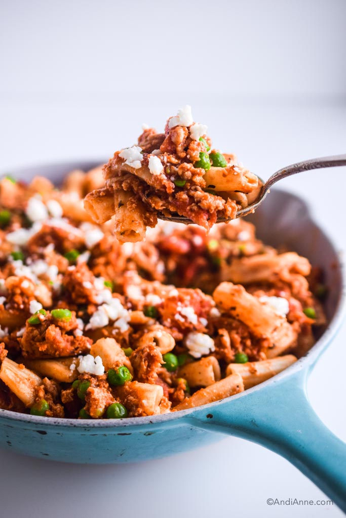 spoon holding rigatoni ground chicken with peas above the blue skillet
