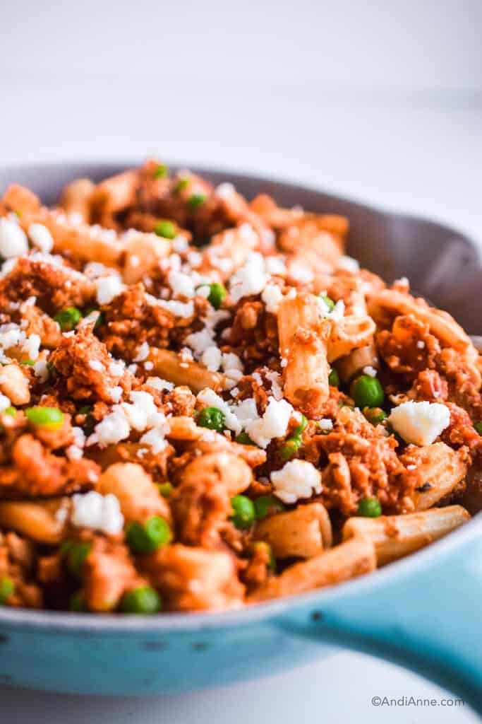 angle shot of rigatoni ground chicken with peas and feta cheese in blue and white skillet