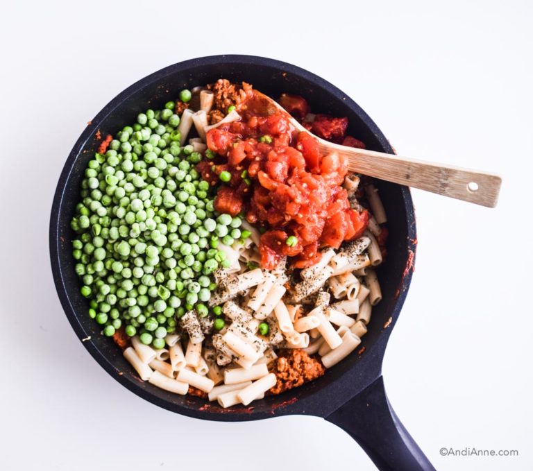 frozen peas, tomatoes, and cooked pasta in a black frying pan