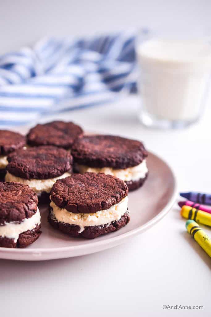 oreo cookies on a pink plate with crayons and milk surrounding it