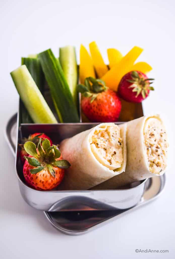 mashed chickpea wraps in kids steel bento lunch box with sliced cucumber, sliced bell peppers, and strawberries.