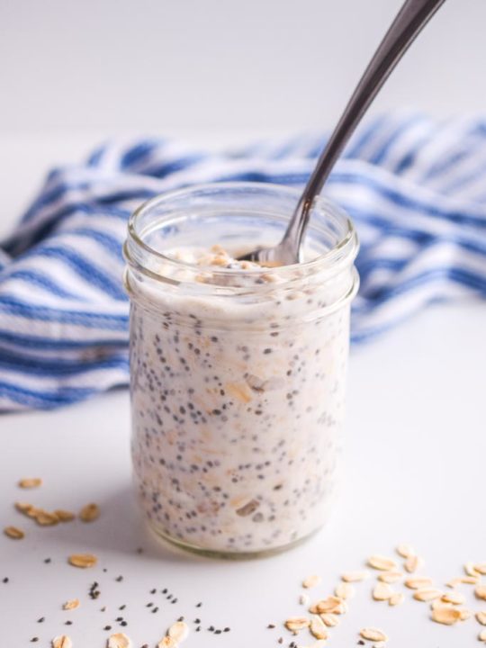 overnight oats with chia seeds in a mason jar with spoon sticking in. Striped blue and white napkin in the background.